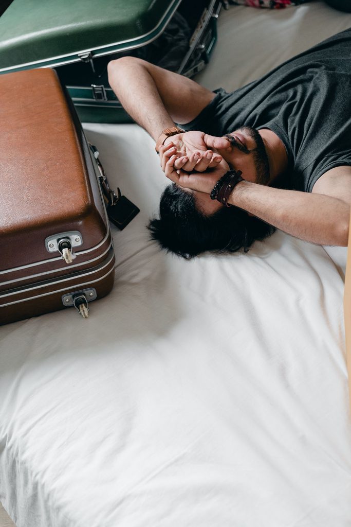homme épuisé sur un lit avec des valises